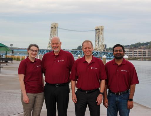 Group photo of four people in front of a bridge